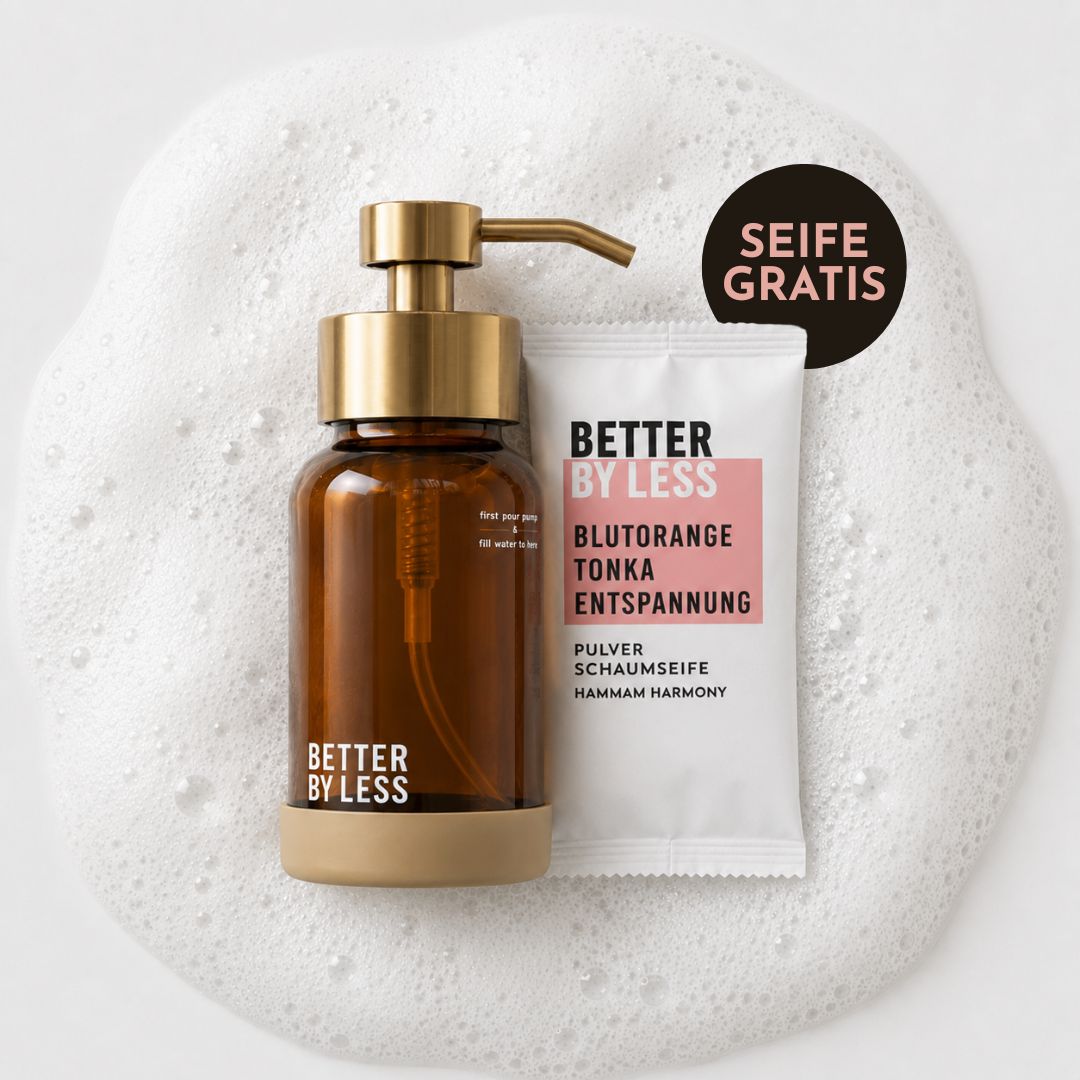 Minimalistisches Produktbild der Better by Less Pulverschaumseife „Hammam Harmony“ mit amberfarbenem Glas-Spender und goldenem Pumpkopf neben weißem Nachfüllsachet auf cremigem Seifenschaum-Hintergrund.